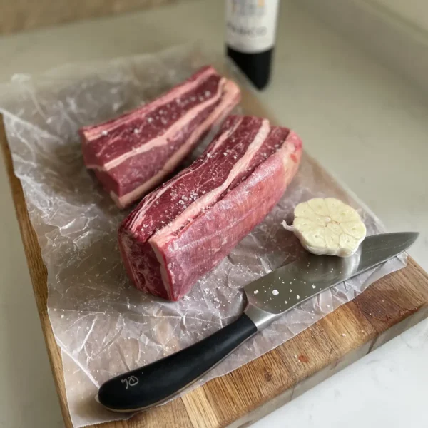Two beef short ribs on a chopping board